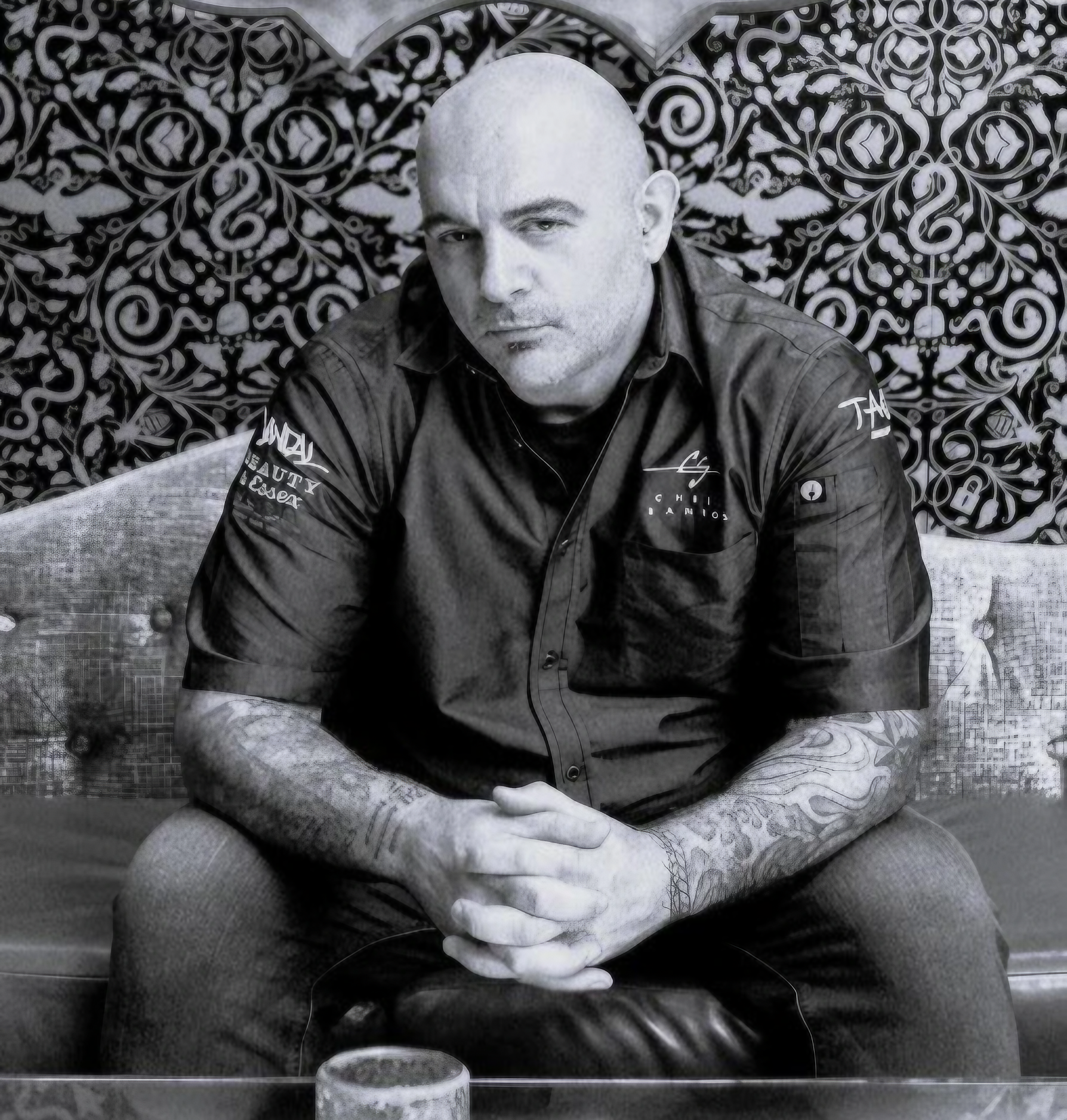 Bald man sitting with tattooed arms crossed.